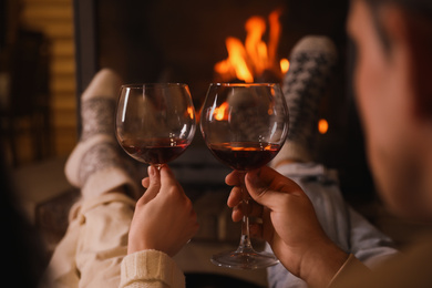 Couple with glasses of red wine near burning fireplace, closeup