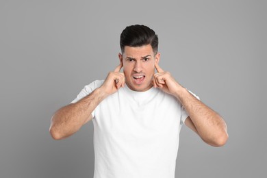 Emotional man covering ears with fingers on grey background