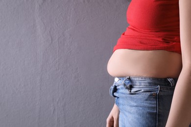 Woman wearing tight clothes on grey background, closeup view with space for text. Overweight problem