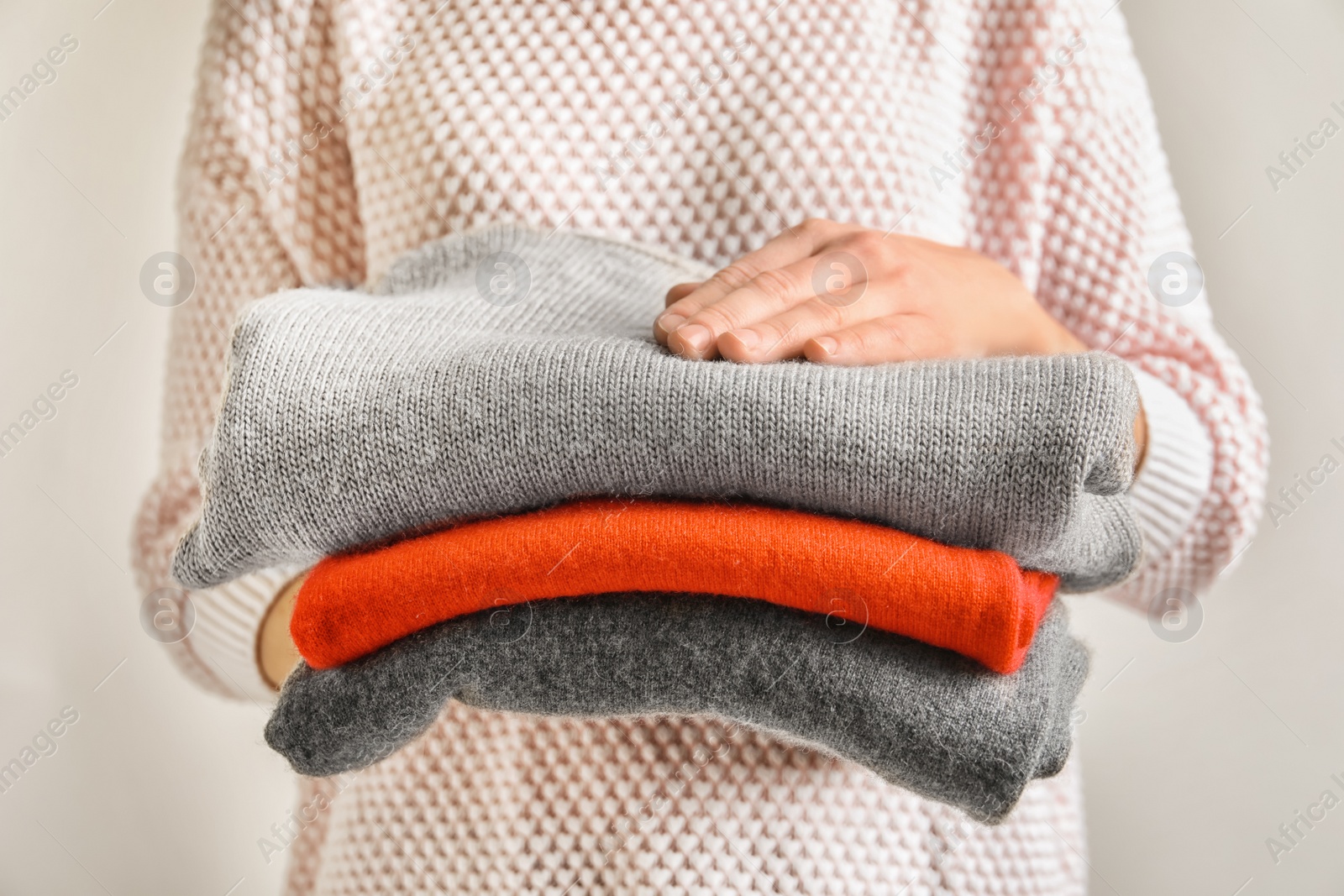 Photo of Young woman holding stack of warm knitted clothes, closeup