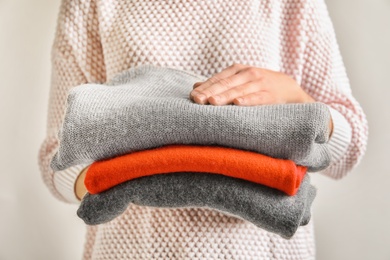 Photo of Young woman holding stack of warm knitted clothes, closeup