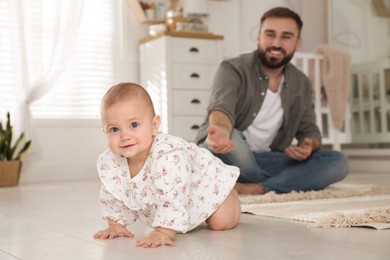 Photo of Happy young father watching his cute baby crawl on floor at home