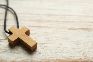 Photo of Christian cross on white wooden table, closeup. Space for text