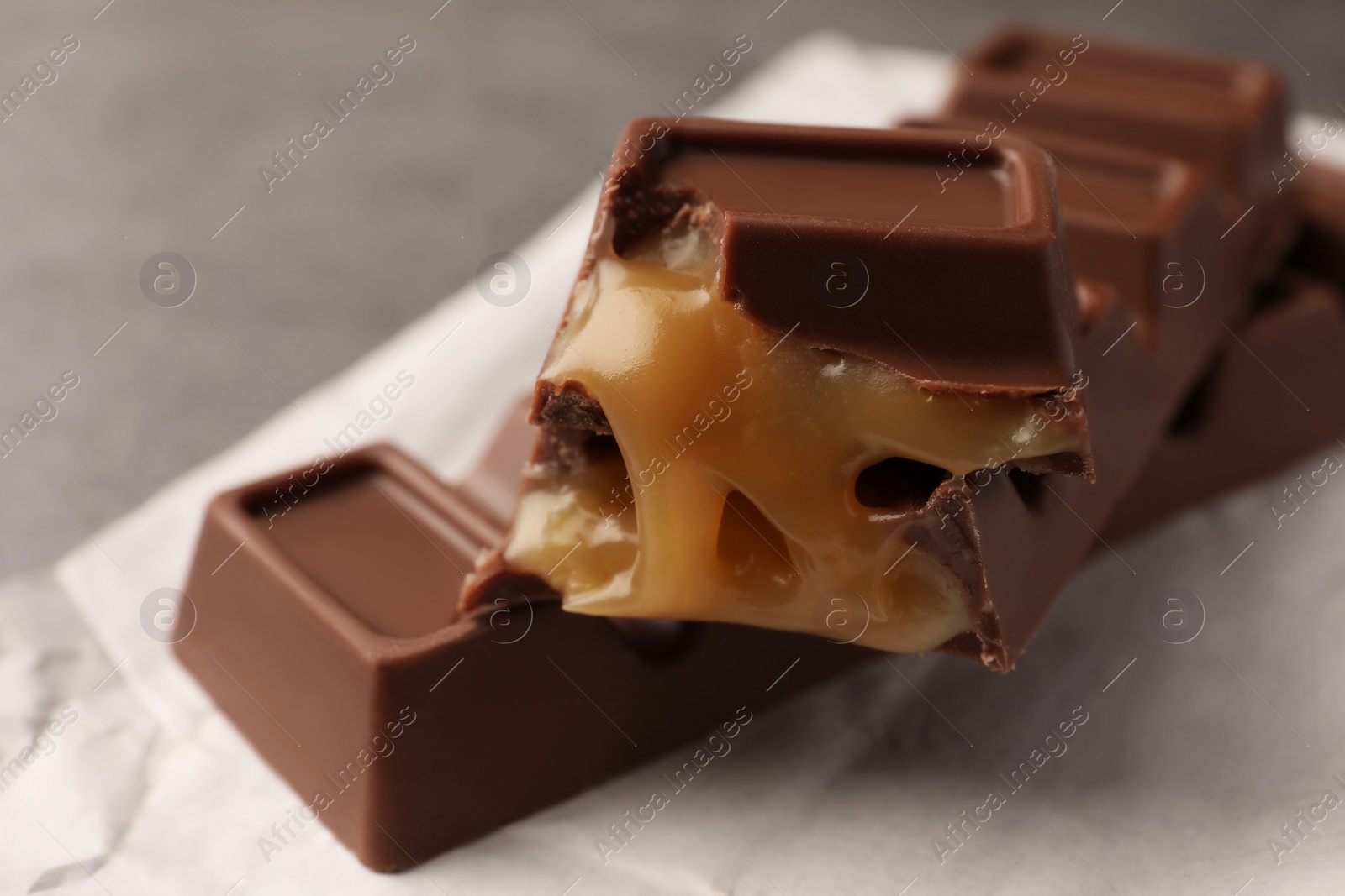 Photo of Tasty sweet chocolate bars with paper wrap on grey table, closeup