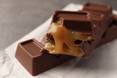 Photo of Tasty sweet chocolate bars with paper wrap on grey table, closeup