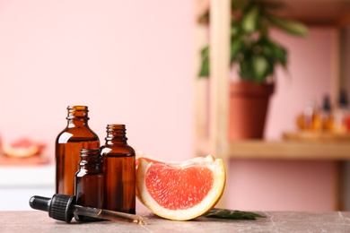 Photo of Bottles of essential oil and grapefruit slices on table against blurred background. Space for text