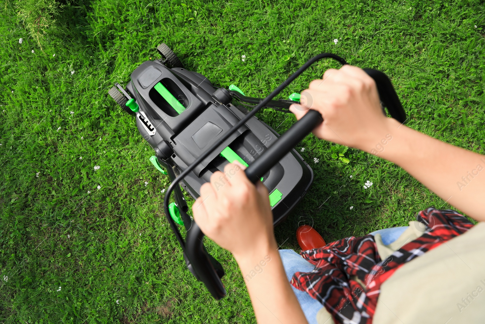 Photo of Above view of woman cutting grass with lawn mower in garden, closeup