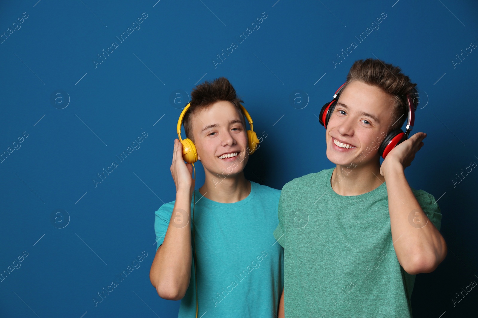 Photo of Teenage twin brothers with headphones on color background