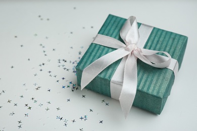 Blue gift box and shiny confetti on light background. Space for text