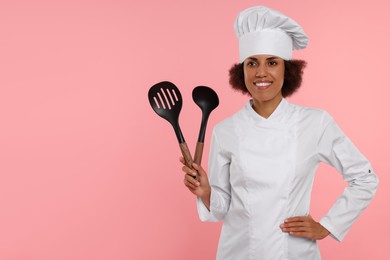 Photo of Happy female chef in uniform holding skimmer and ladle on pink background. Space for text
