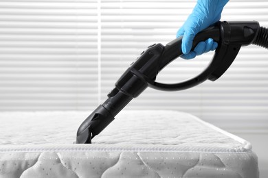 Photo of Person disinfecting mattress with vacuum cleaner indoors, closeup