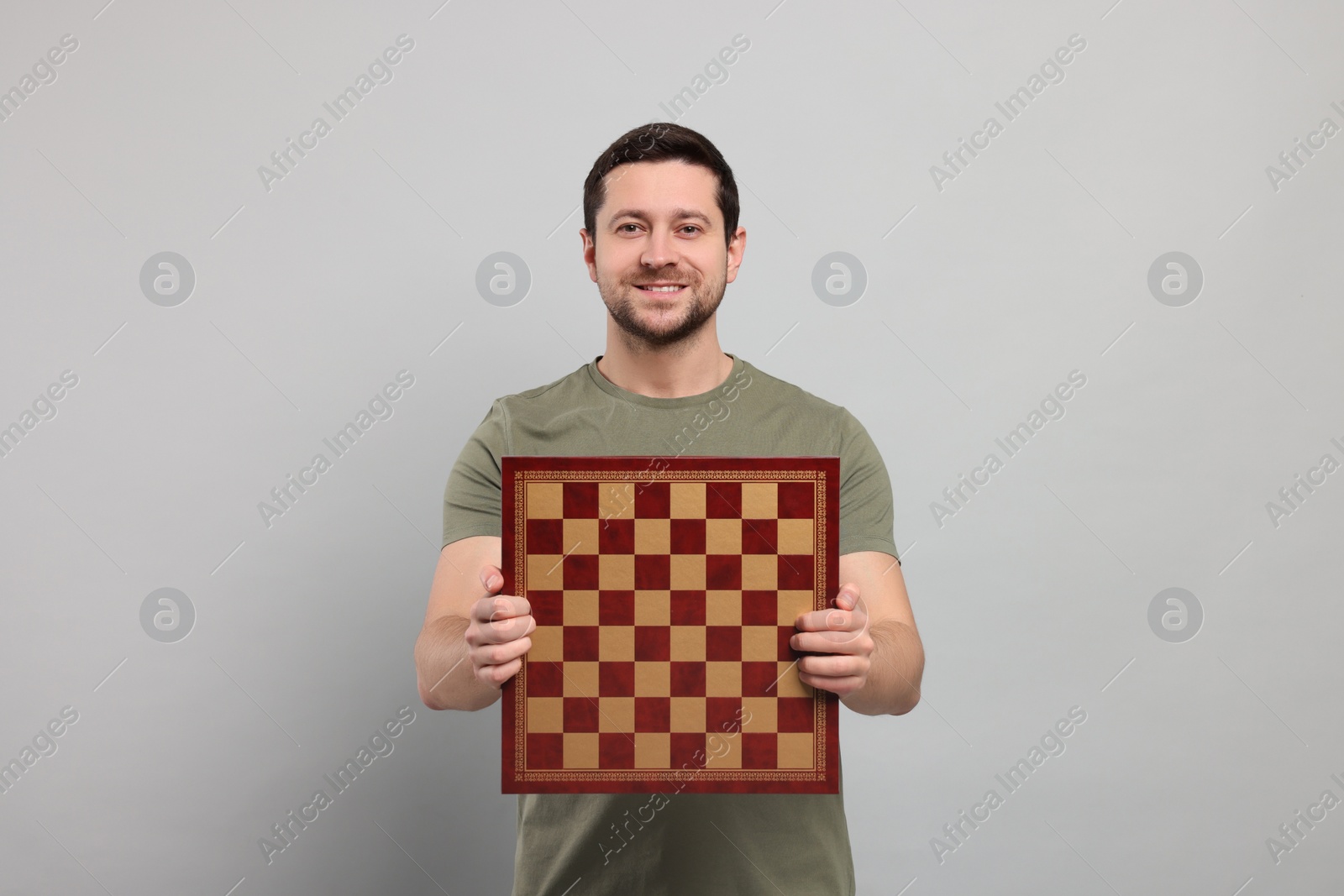 Photo of Handsome man holding chessboard on light grey background