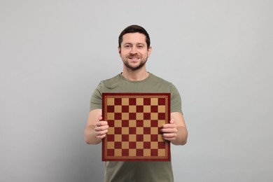 Handsome man holding chessboard on light grey background