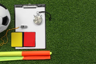Soccer ball and different referee equipment on green grass, flat lay. Space for text