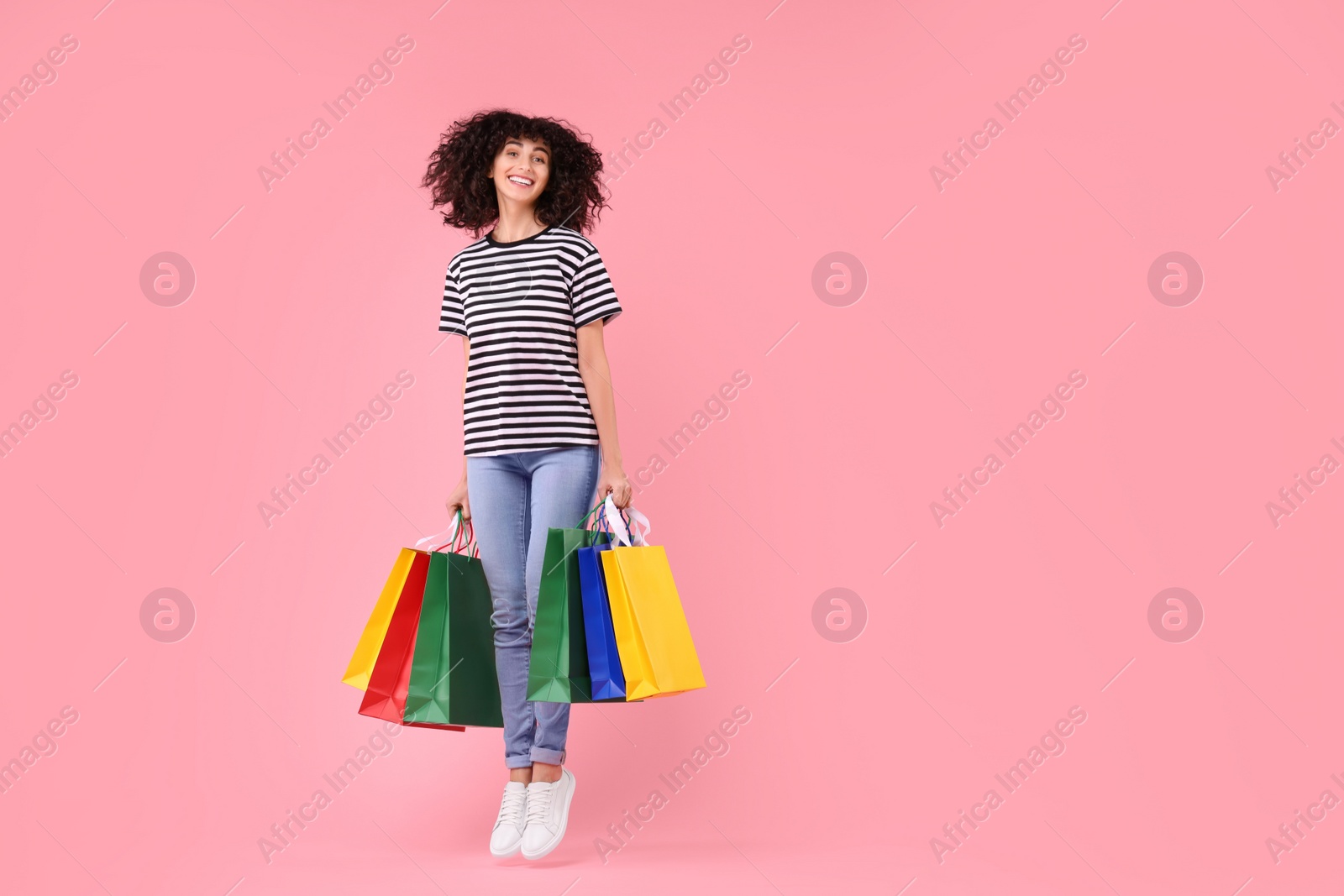 Photo of Happy young woman with shopping bags on pink background