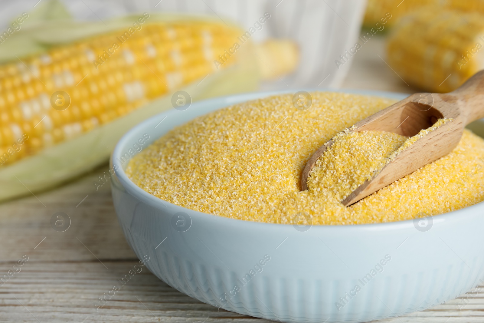 Photo of Cornmeal in bowl and fresh cobs on white wooden table, closeup