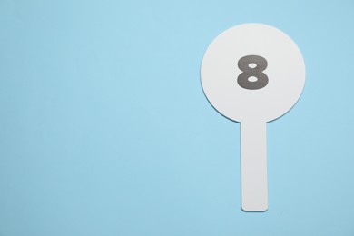 Photo of Auction paddle with number 8 on light blue background, top view. Space for text