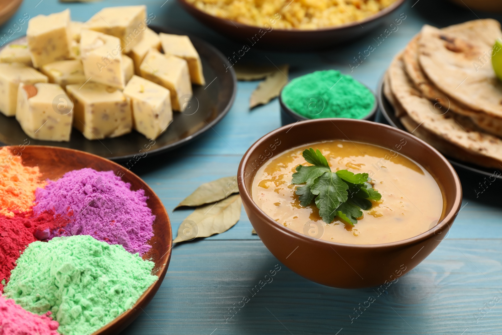 Photo of Traditional Indian food and color powders on light blue wooden table. Holi festival celebration