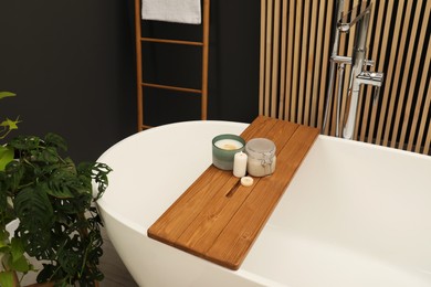 Photo of Spa day. Candles and cosmetic product on wooden tub tray in bathroom