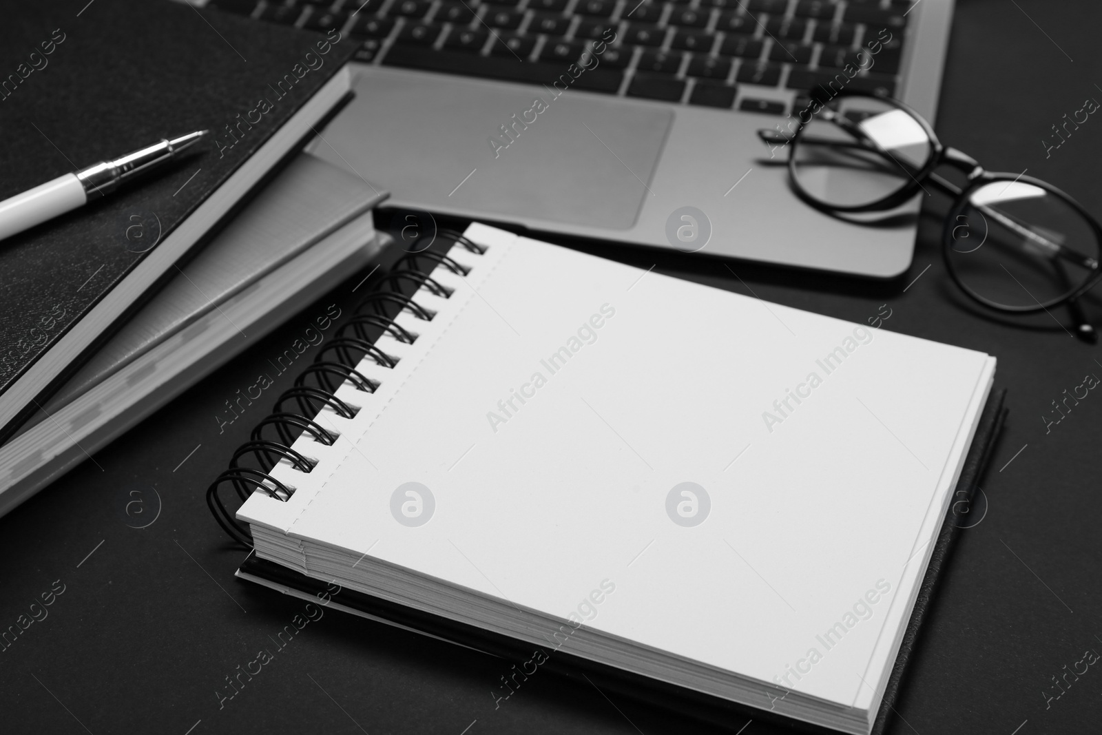 Photo of Notebooks, laptop, glasses and pen on black table
