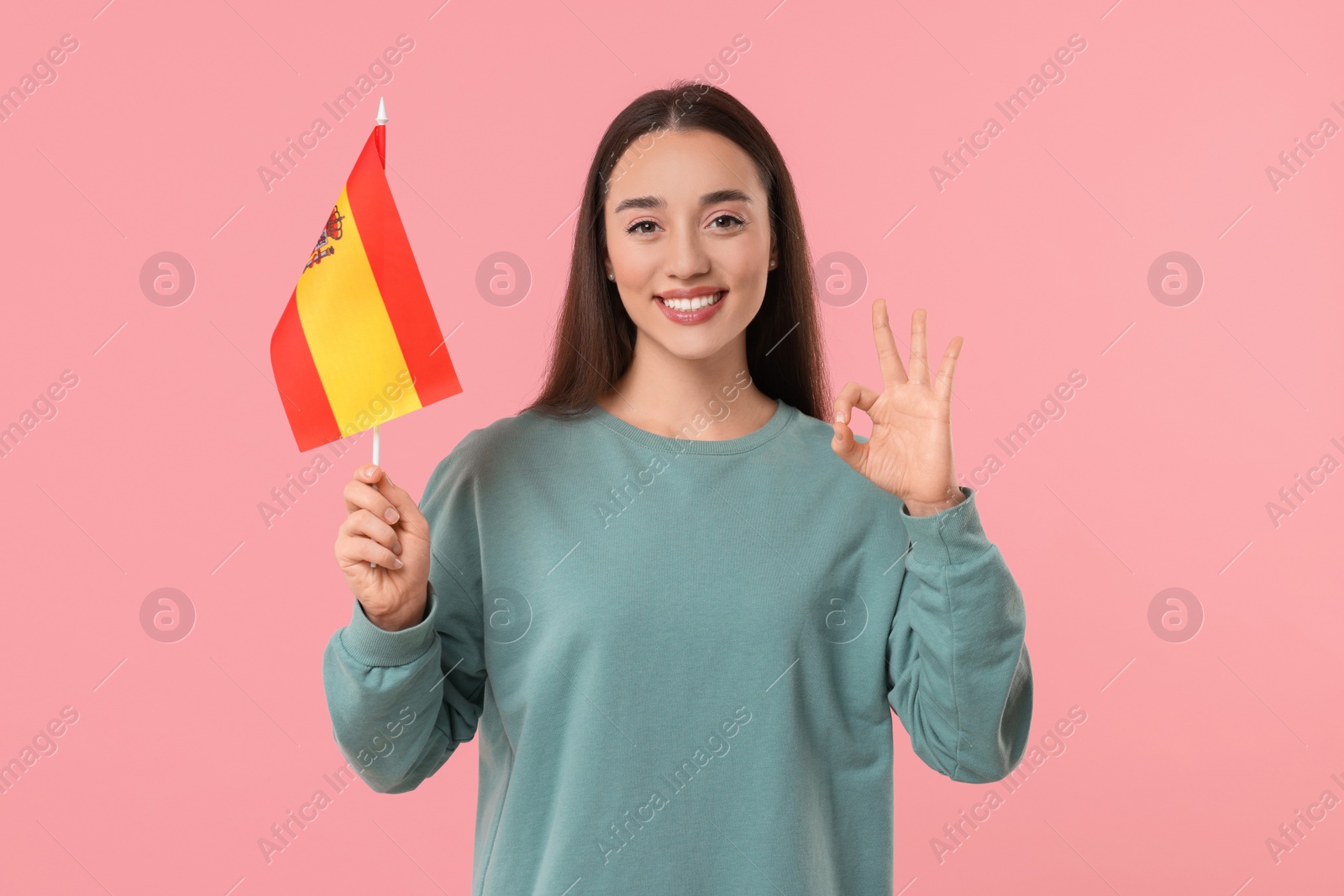 Photo of Young woman with flag of Spain showing ok gesture on pink background