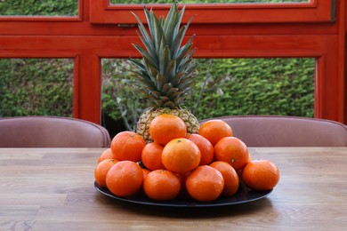 Photo of Fresh tangerines and pineapple on wooden table indoors