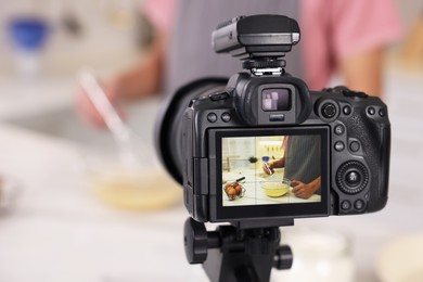 Photo of Food blogger cooking while recording video in kitchen, focus on camera