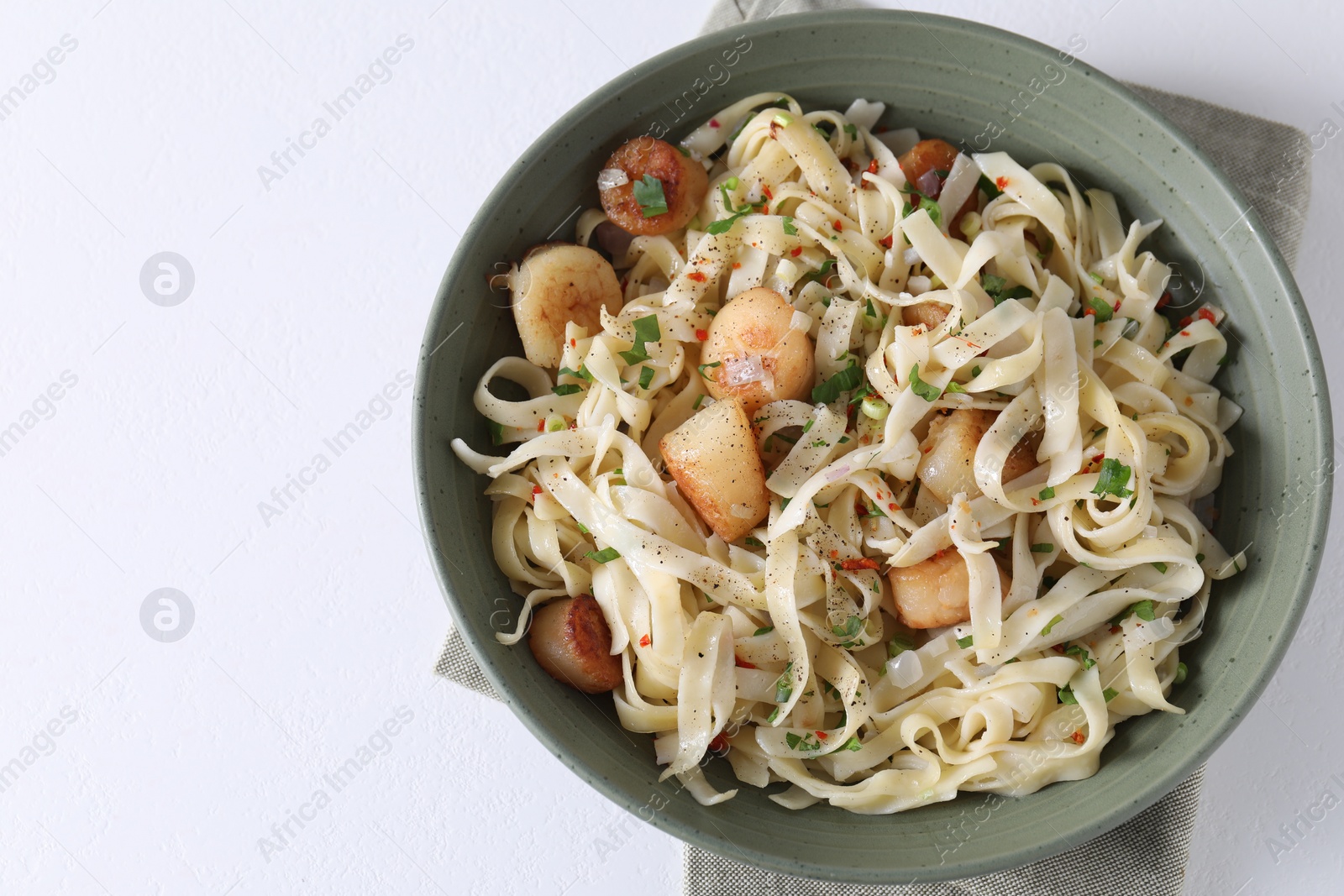 Photo of Delicious scallop pasta with spices in bowl on white table, top view. Space for text