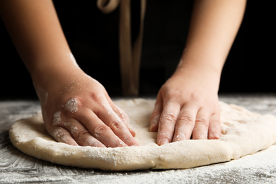 Photo of Woman kneading dough for pizza at grey table, closeup