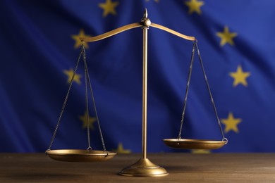 Photo of Scales of justice on wooden table against European Union flag