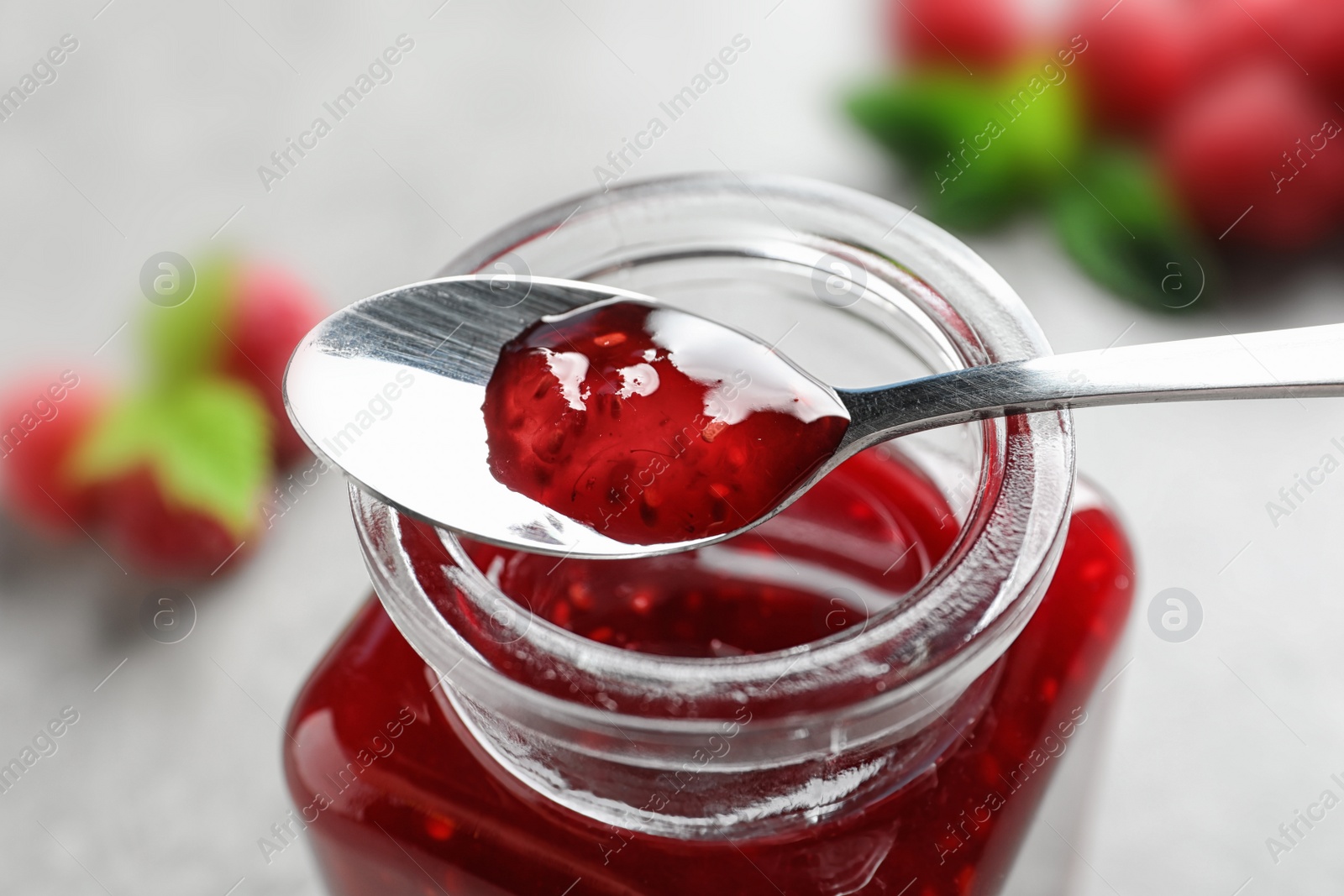 Photo of Glass jar and spoon of sweet raspberry jam on table, closeup