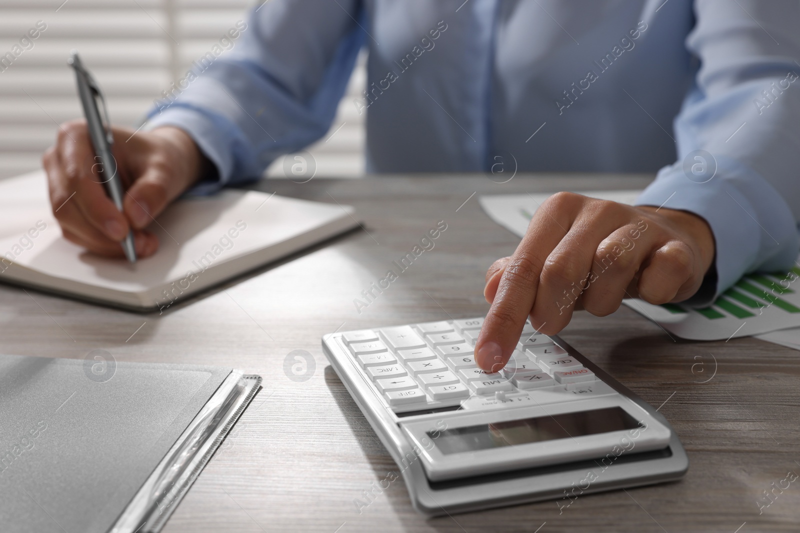 Photo of Woman using calculator at light wooden table in office, closeup