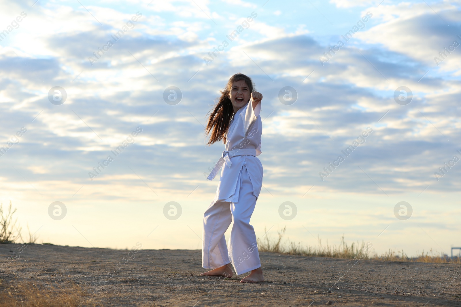 Photo of Cute little girl in kimono practicing karate outdoors