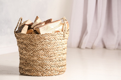 Photo of Wicker basket with cut firewood on white floor indoors