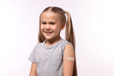 Happy girl with sticking plaster on arm after vaccination against white background