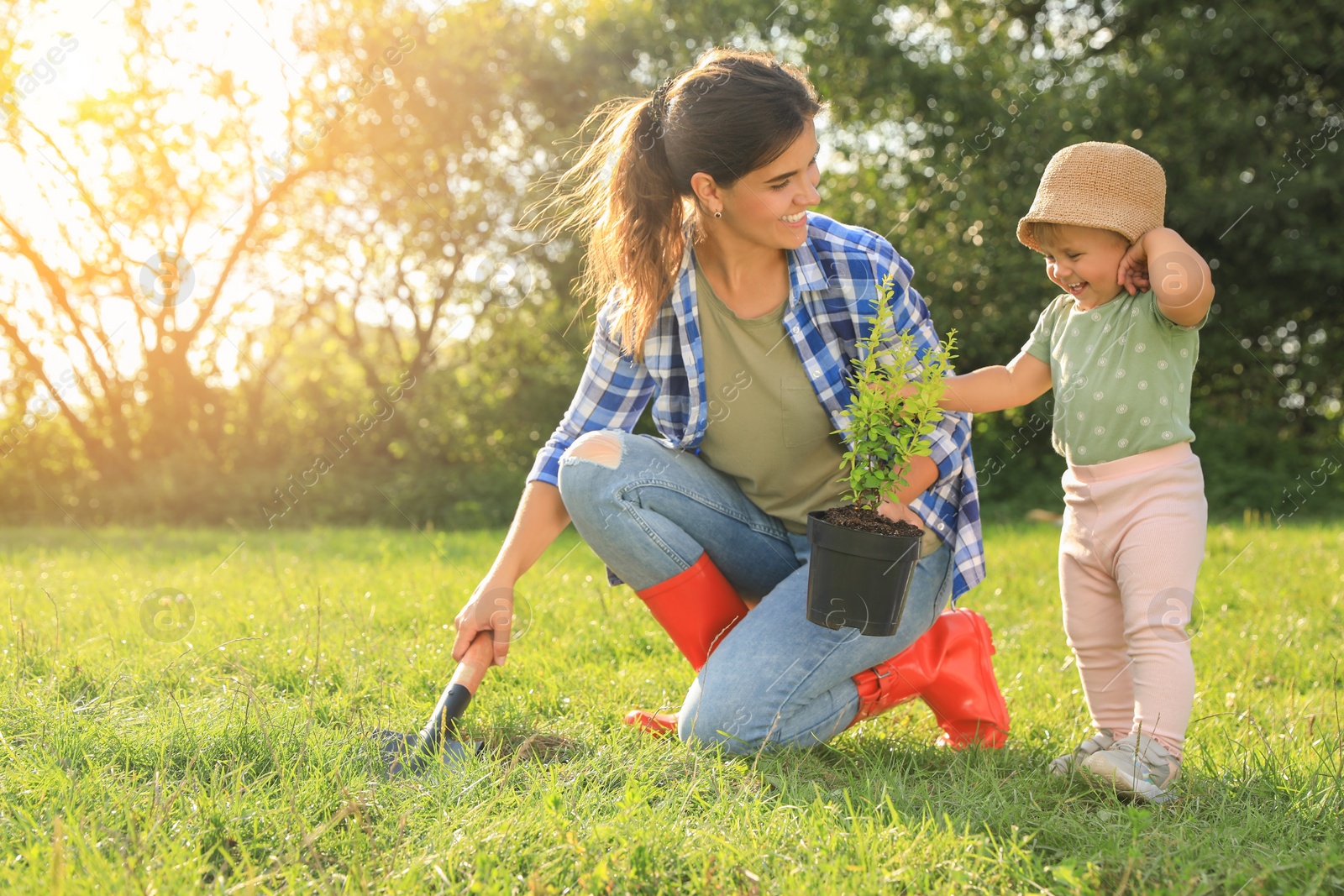 Photo of Mother and her baby daughter planting tree together in garden