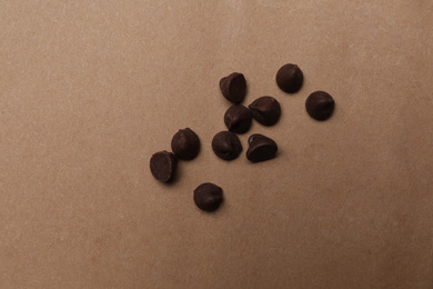 Delicious chocolate chips on brown background, top view