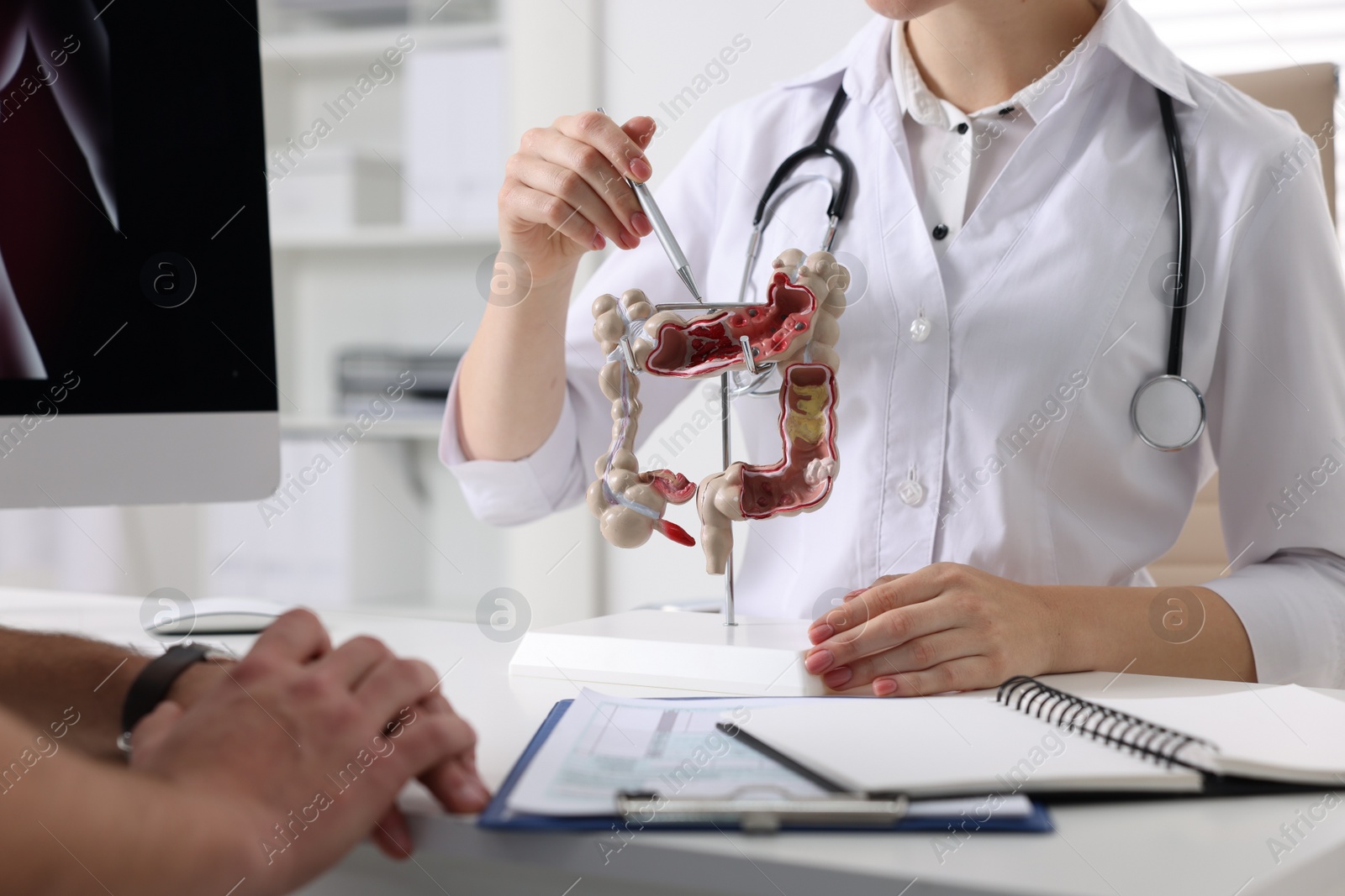 Photo of Gastroenterologist with anatomical model of large intestine consulting patient at table in clinic, closeup