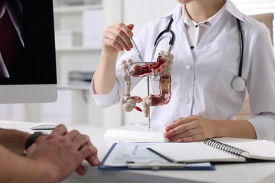 Gastroenterologist with anatomical model of large intestine consulting patient at table in clinic, closeup