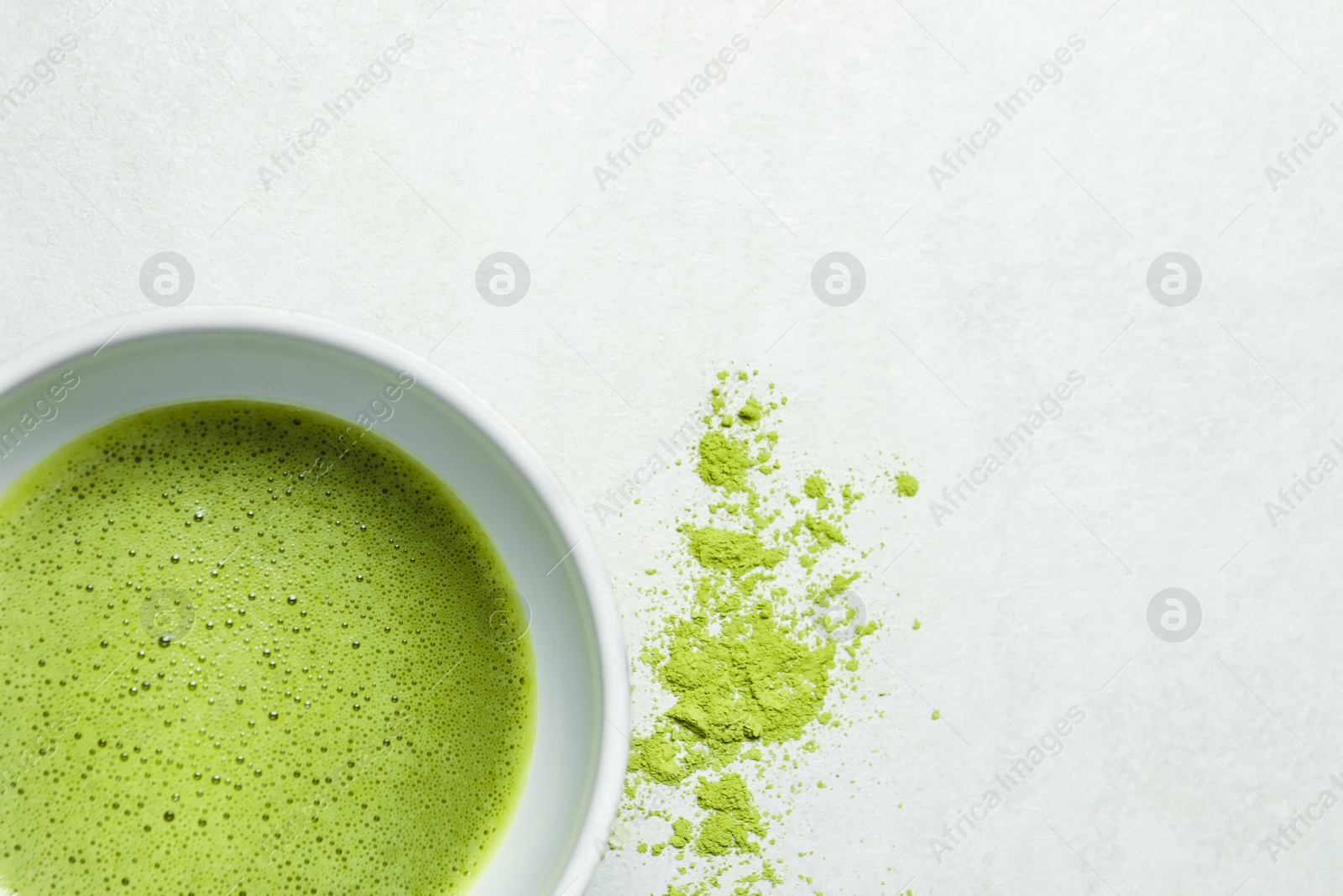 Photo of Cup of fresh matcha tea and green powder on light grey table, top view. Space for text