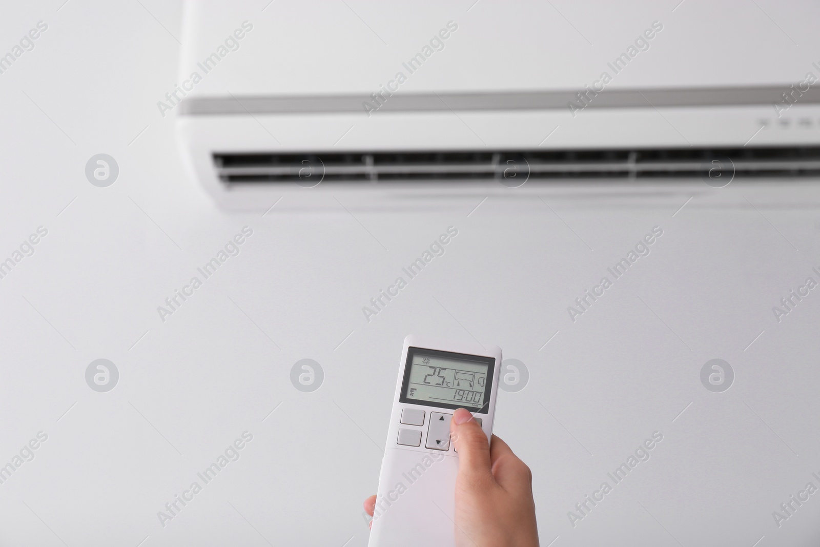 Photo of Woman operating air conditioner with remote control indoors, focus on hand