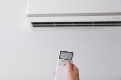 Woman operating air conditioner with remote control indoors, focus on hand