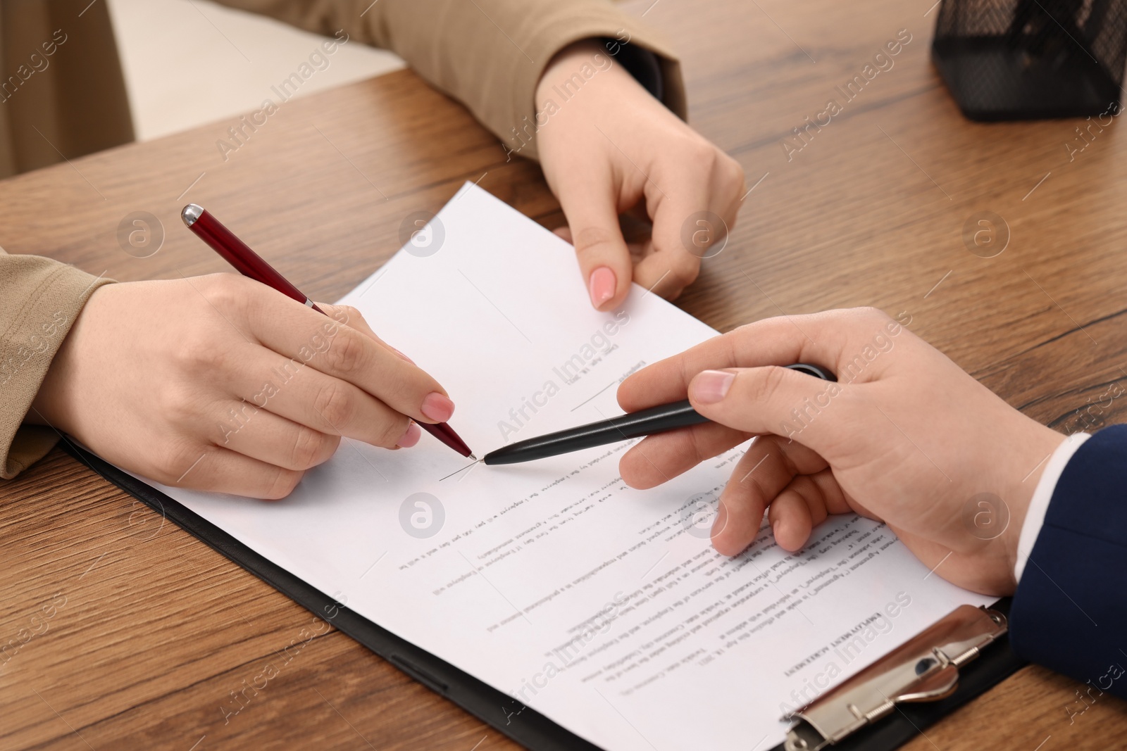 Photo of Man pointing at document and woman putting signature at wooden table, closeup