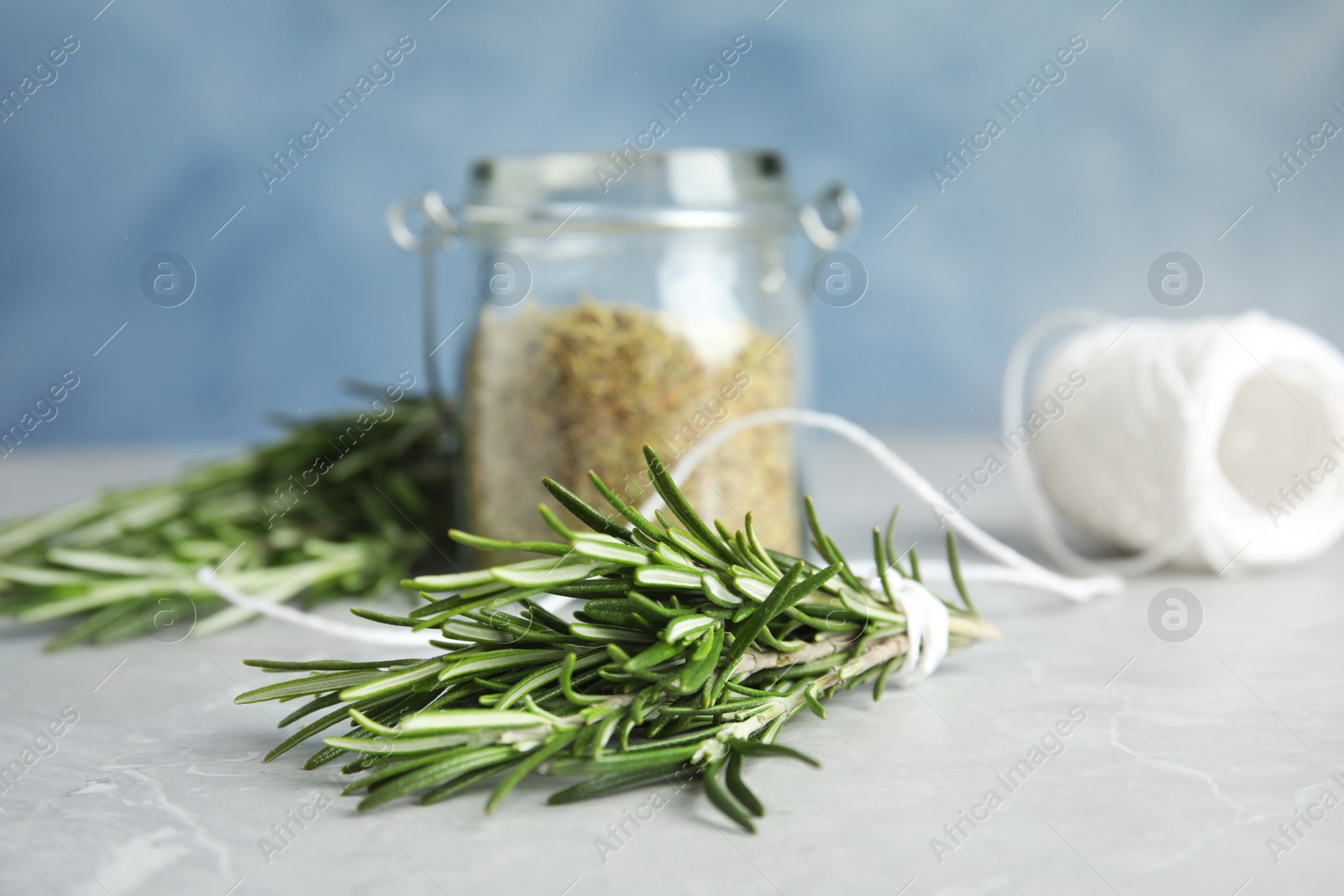 Photo of Jar with dried rosemary, twine and fresh twigs on table