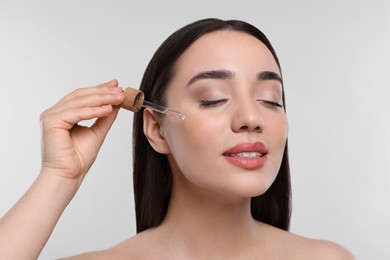 Photo of Young woman applying essential oil onto face on white background, closeup