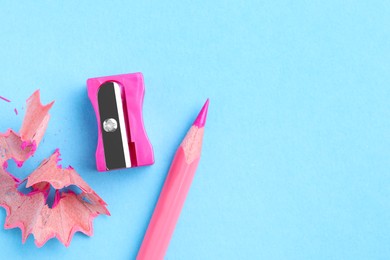 Photo of Pink pencil, sharpener and shavings on light blue background, flat lay. Space for text