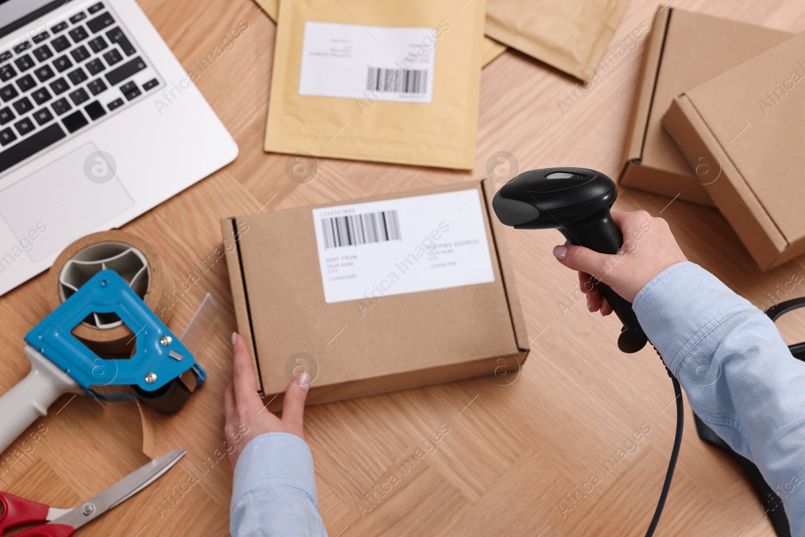 Photo of Parcel packing. Post office worker with scanner reading barcode at wooden table, top view