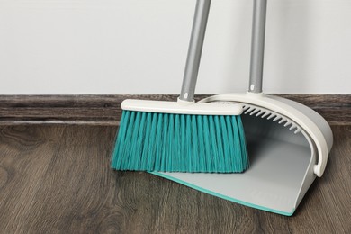 Photo of Plastic broom with dustpan on wooden floor indoors