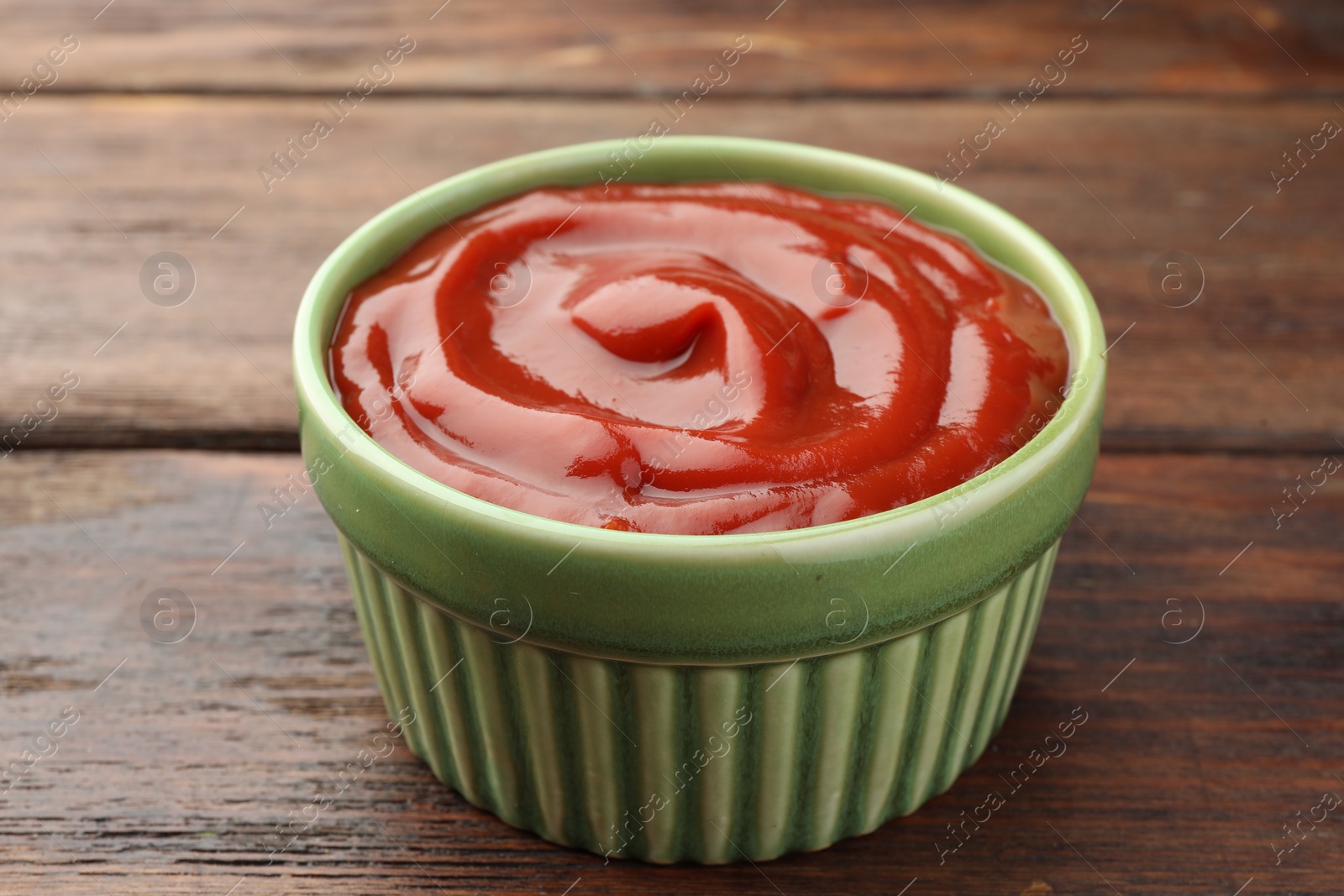 Photo of Bowl of tasty ketchup on wooden table, closeup