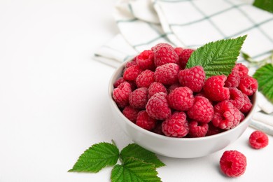Photo of Bowl of fresh ripe raspberries with green leaves on white table. Space for text
